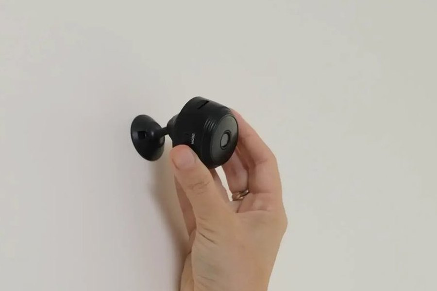 Hand mounting the compact Home Defender Cam security camera on a wall with its swivel base