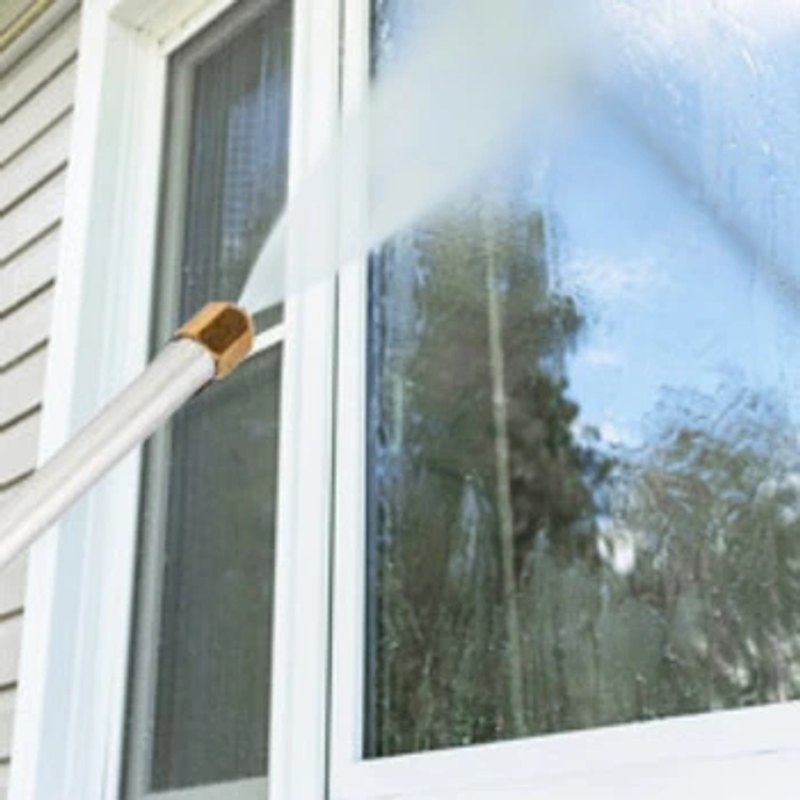 A person using the HydroBlast Power Nozzle to spray and clean an exterior window