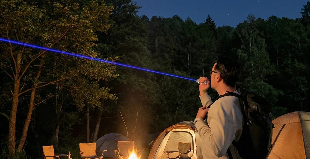 Person outdoors at night aiming the IgniteBeam handheld blue laser, showing a visible blue beam