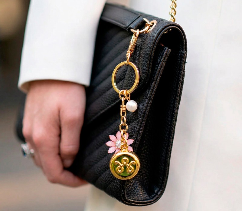 Gold invisaWear safety keychain charm clipped to a black leather handbag