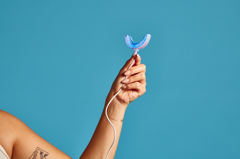 Hand holding the LaughLand LED whitening mouthpiece with its phone cable