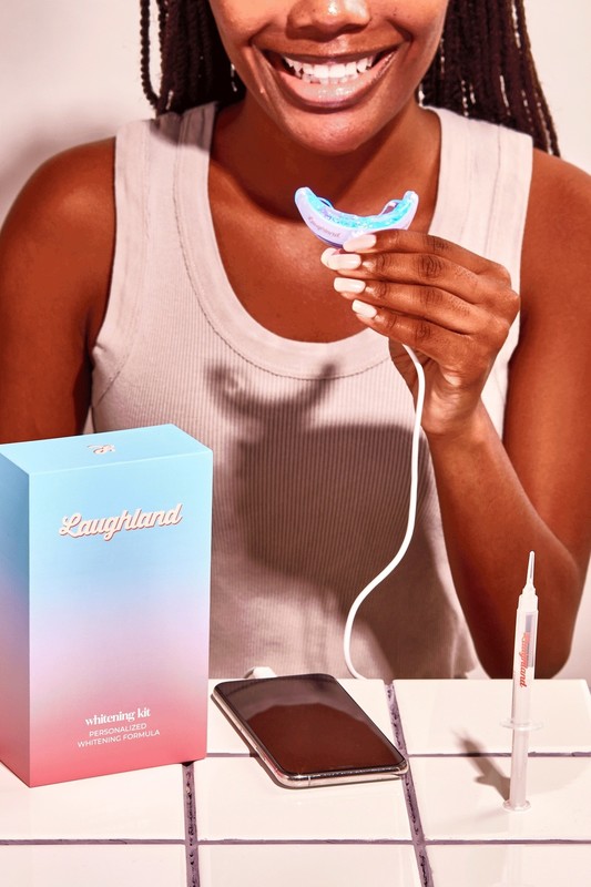 Person holding the LaughLand LED whitening mouthpiece beside the kit box