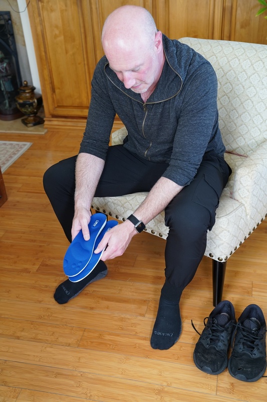 Person placing a blue Liftly insole into a shoe while sitting in a chair