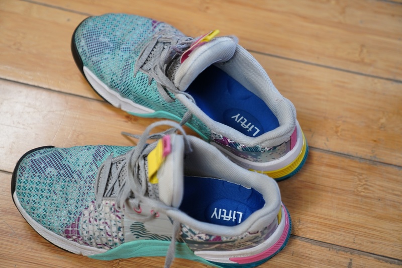 Liftly insoles fitted inside a pair of colorful running shoes on a wood floor