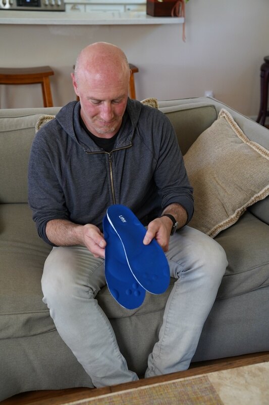 A person holding a blue Liftly cushioned insole while seated