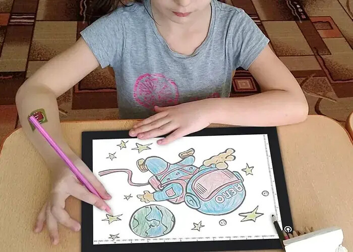 A child tracing an astronaut drawing on the lit Lite Sketch Lightpad