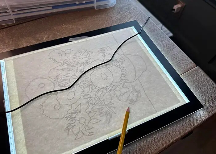 A floral stencil being traced on the lit Lite Sketch Lightpad with a pencil