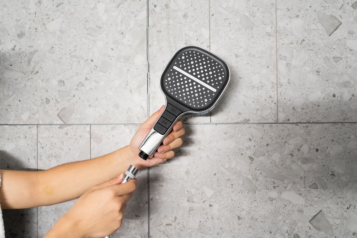 Hands attaching the Maas & Bath Showerhead to a shower hose against a tiled wall