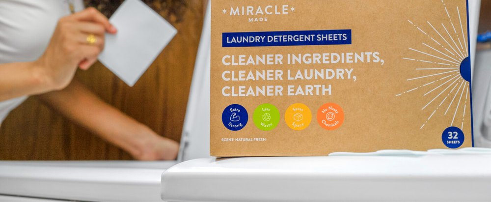 A person holding a Miracle detergent sheet beside a washing machine with the box