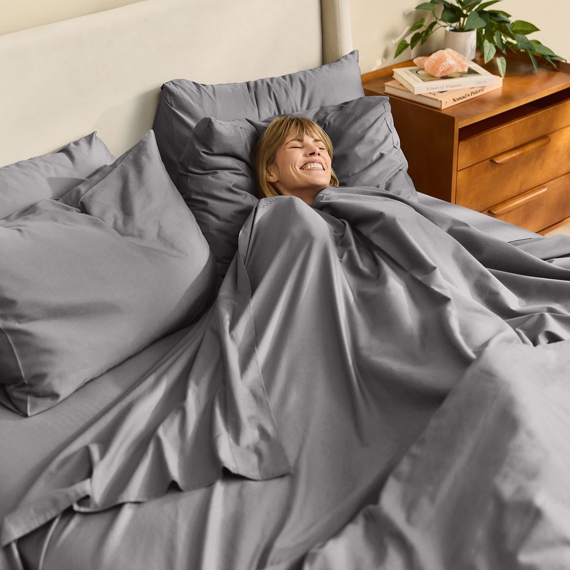 Smiling woman tucked into Stone Grey Miracle Made sheets