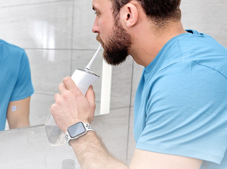 Man using the Miracle Smile cordless water flosser in front of a bathroom mirror