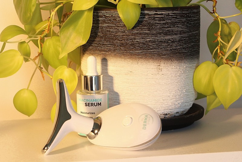 The MyoGlow LED skin-sculpting wand standing on a shelf beside a serum bottle and a plant