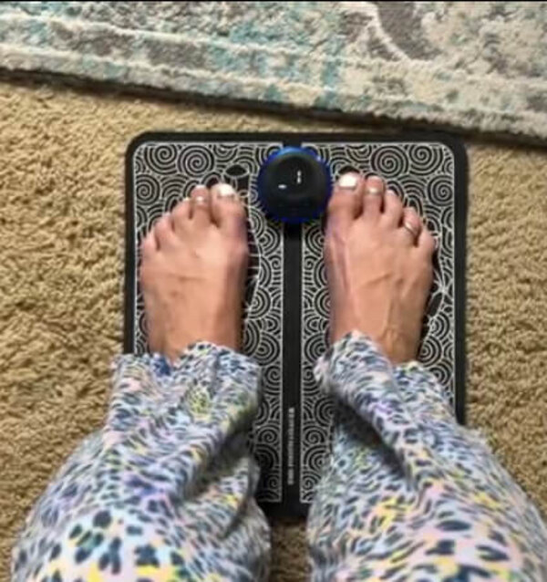 Person resting both bare feet on the Nooro Foot Massager mat during a session