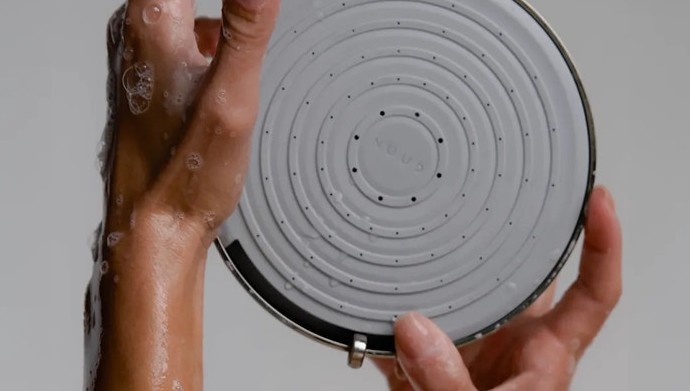 Hands holding the round, low-profile spray face of the NUUD filtered showerhead
