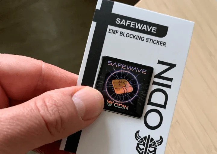 Hand holding the ODIN SafeWave EMF Blocking Sticker on its retail card