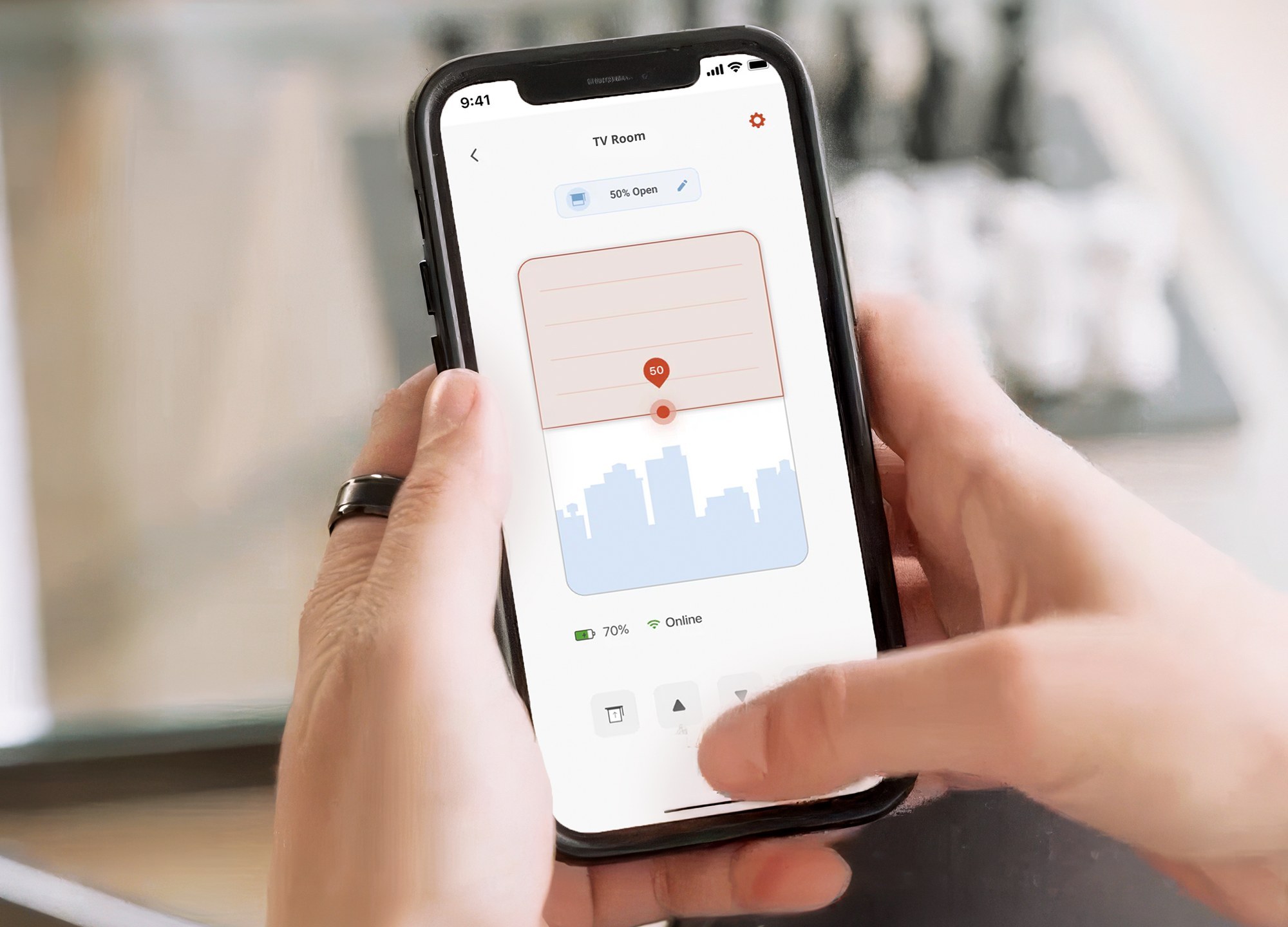 A hand holding a phone that shows the RYSE app controlling a shade set to 50 percent open with a battery reading