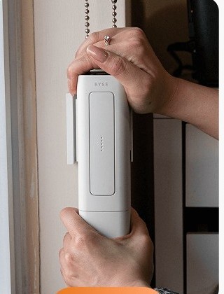 Hands mounting the RYSE SmartShade motor onto a window bracket with the beaded chain running through it