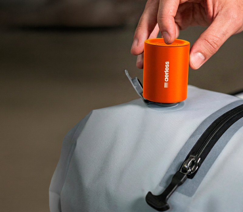 Hand placing the orange Aerless rechargeable pump on a vacuum bag's valve to compress it