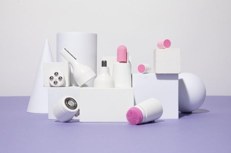 The Pluxy epilator, cleansing brush, and grooming attachment heads arranged on white display blocks
