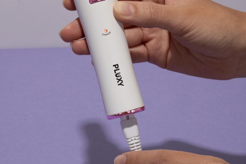 Hand holding the Pluxy epilator while plugging in the USB charging cable