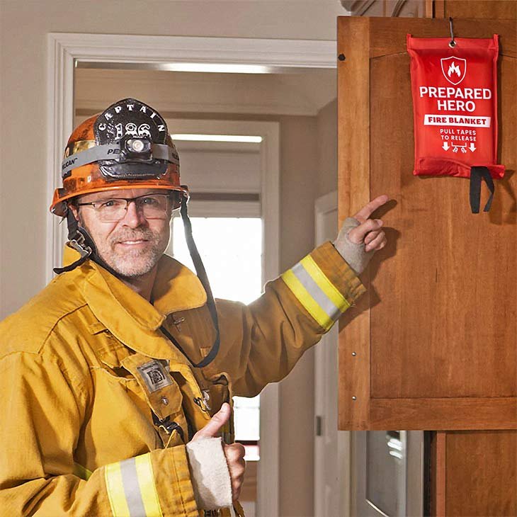 Firefighter pointing at a Prepared Hero fire blanket mounted on a kitchen cabinet