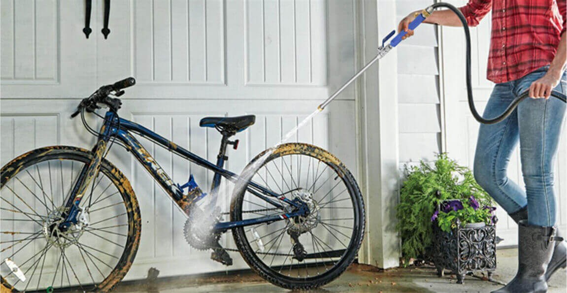 A person using the PressurePro Power Nozzle wand to rinse a muddy bike