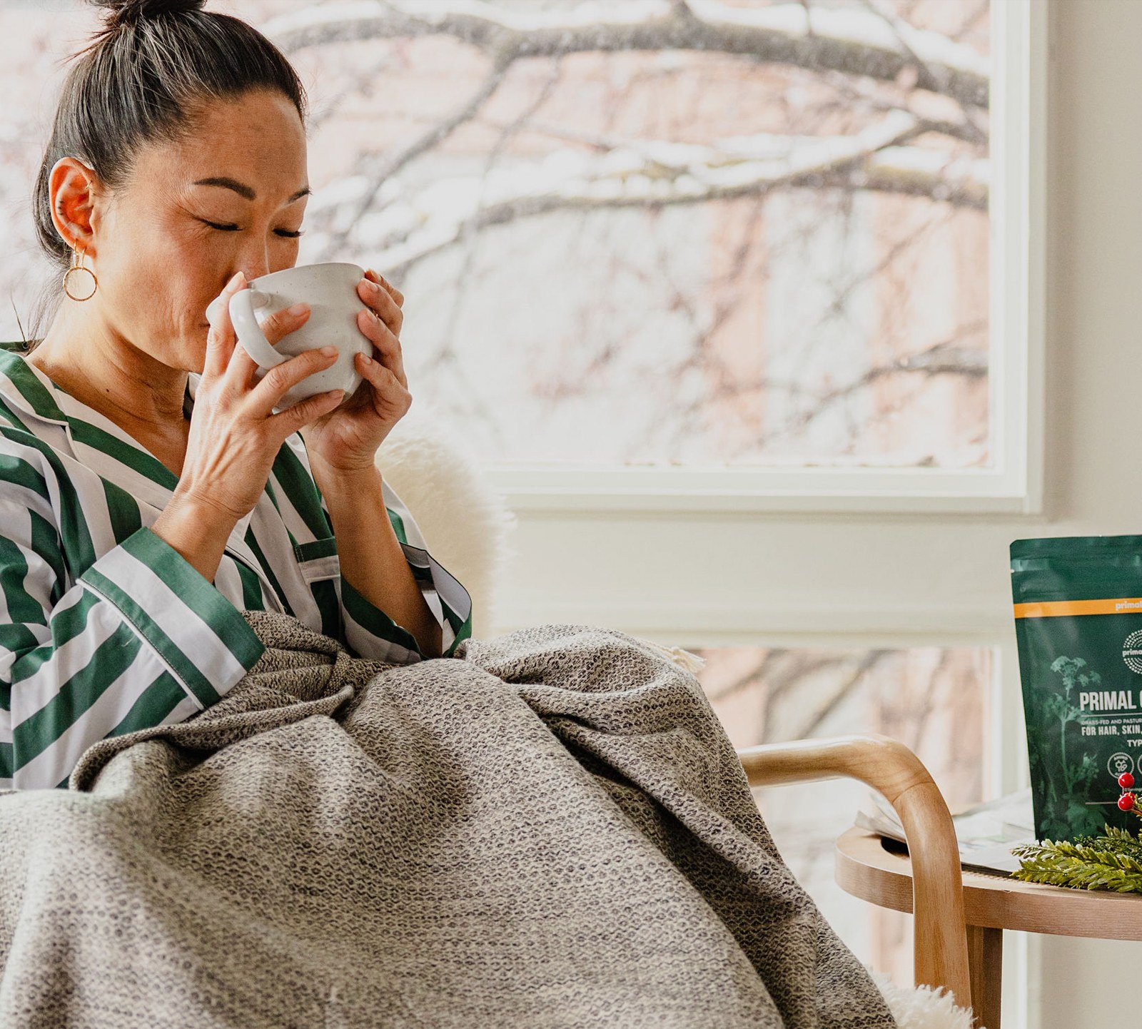 A person drinking from a mug with a Primal Collagen pouch on a side table