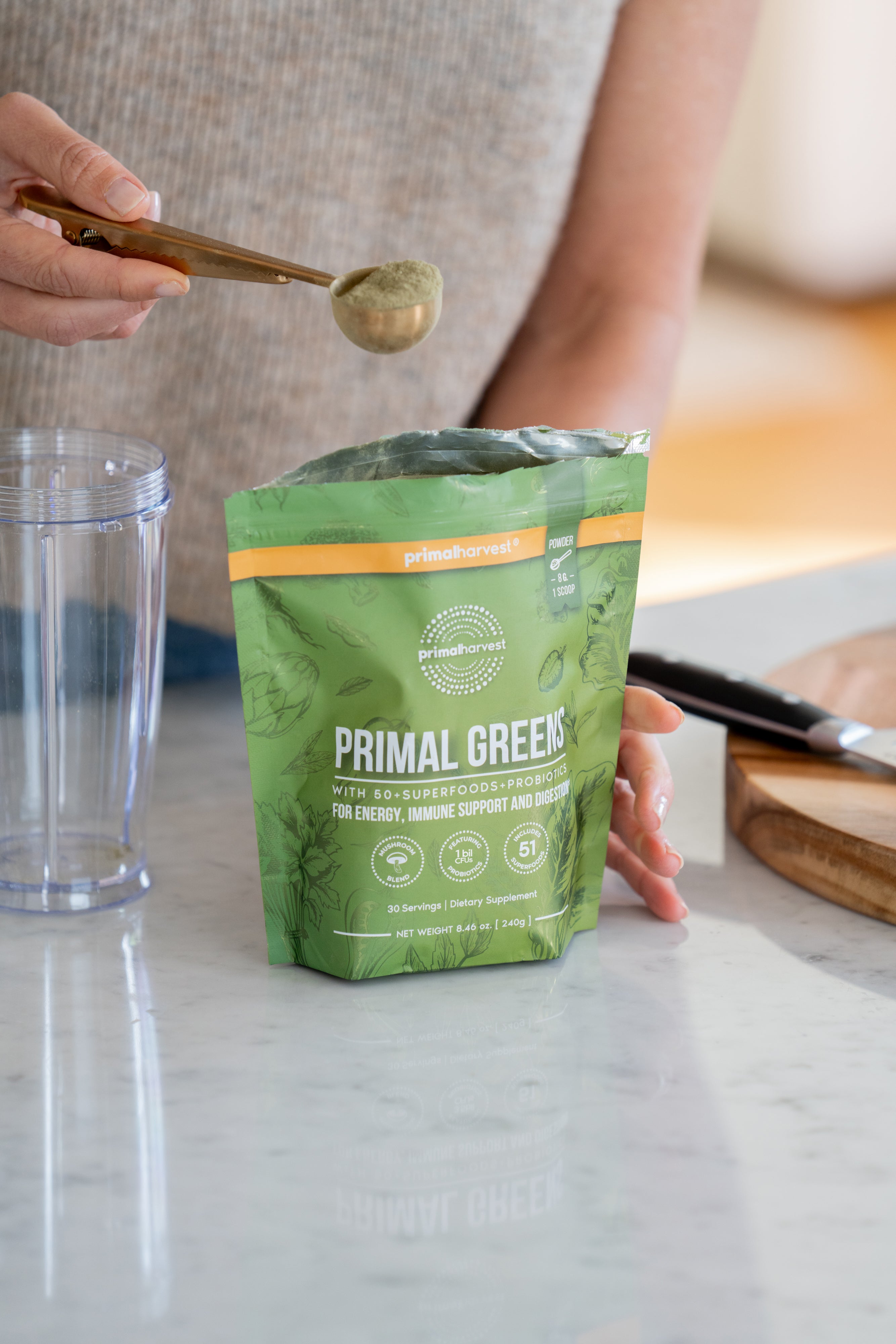 Primal Greens super-greens powder being scooped from the pouch into a blender cup