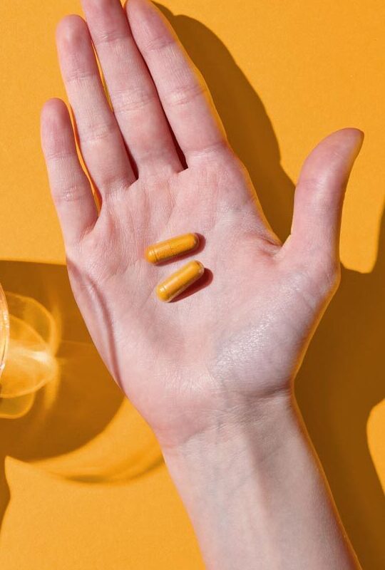Two Primal Turmeric Complex capsules held in an open palm