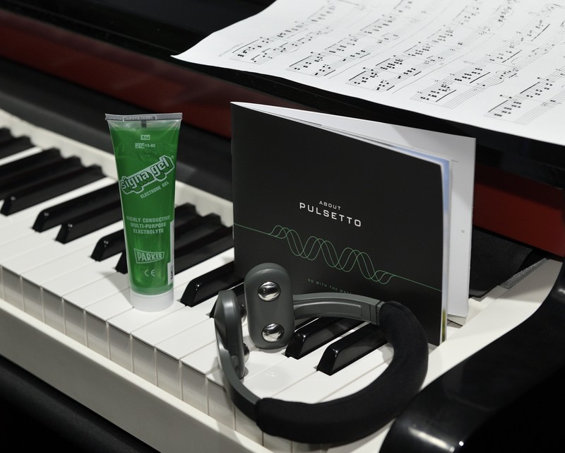 The Pulsetto vagus nerve stimulator next to its conductive gel tube and About Pulsetto booklet