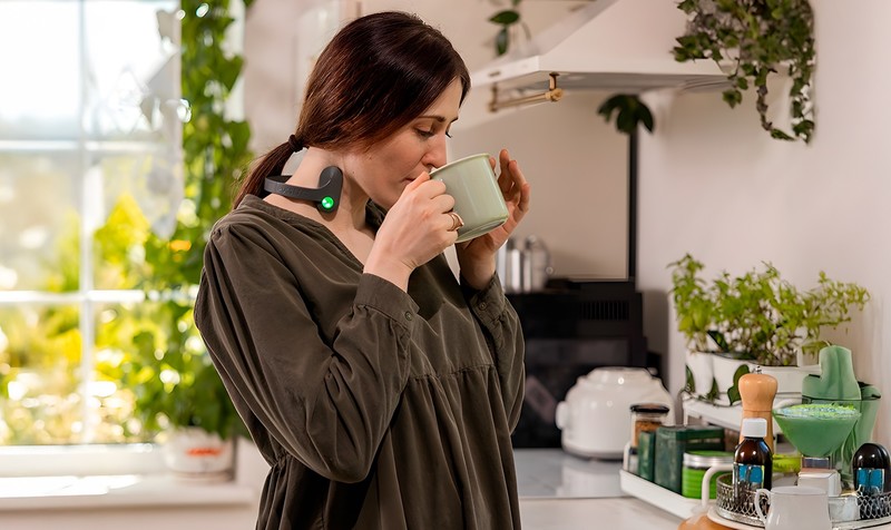 Person wearing the Pulsetto vagus nerve stimulator around the neck while holding a mug in a kitchen