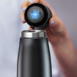 A hand holding the Pura UV Smart Bottle with the UV-C cap glowing blue during a cleaning cycle