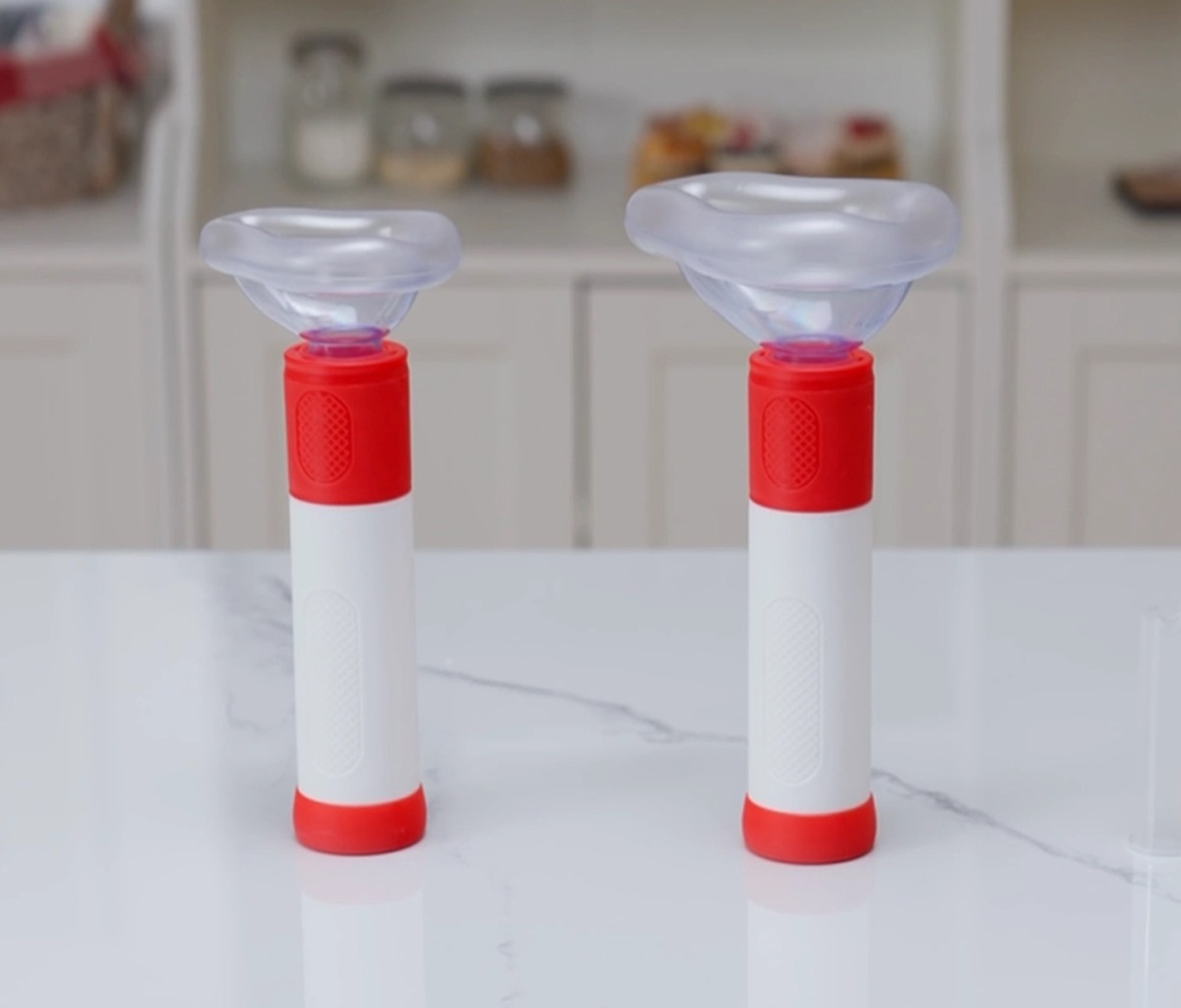Two ResQVac anti-choke devices on a kitchen counter, one fitted with the child mask and one with the adult mask