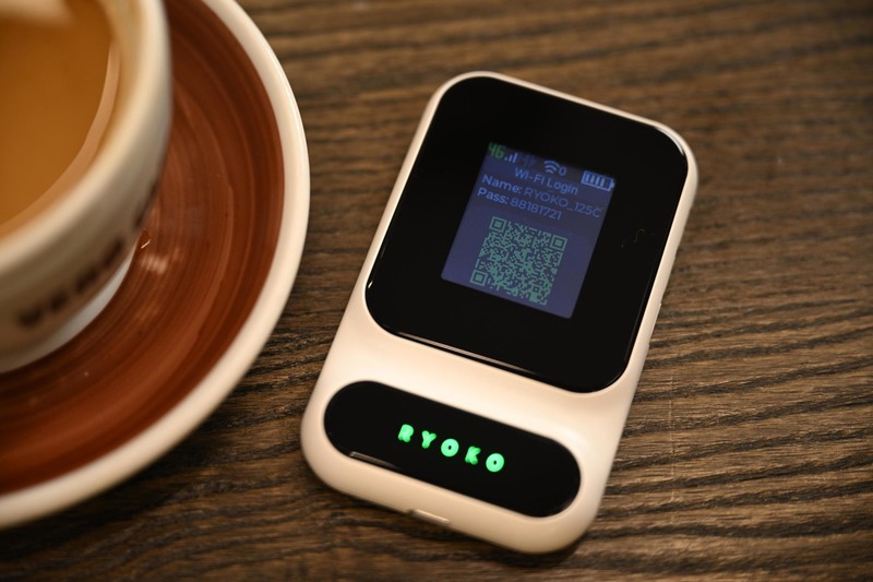 Ryoko Pro portable WiFi hotspot on a wooden table beside a cup of coffee, its screen lit