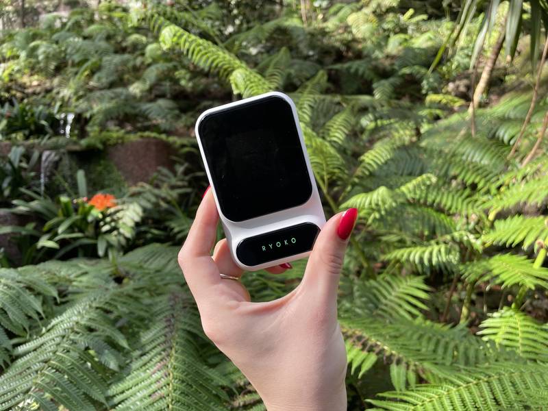 Person holding the Ryoko Pro portable WiFi hotspot outdoors while traveling
