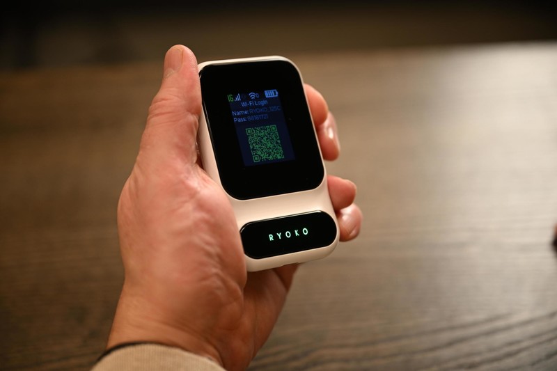 Ryoko Pro portable WiFi hotspot held in one hand with its screen showing the WiFi network login
