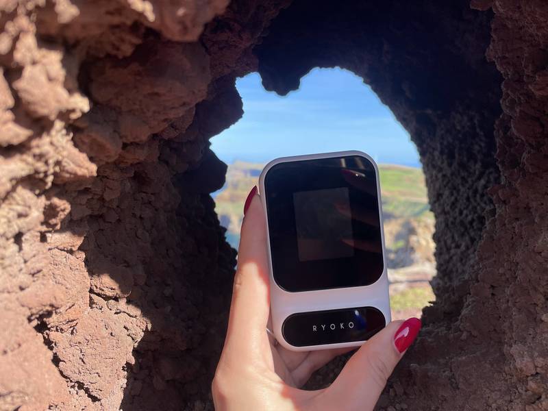 Person holding the Ryoko Pro portable WiFi hotspot outdoors while traveling