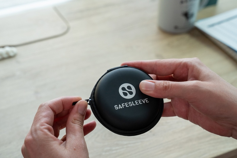 Hands opening the round zippered SafeSleeve carry case for the air tube headphones on a wooden desk