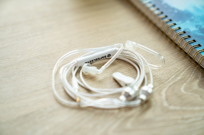 Close-up of the SafeSleeve air tube headphones showing the clear acoustic tubes, aluminum earpieces and inline control