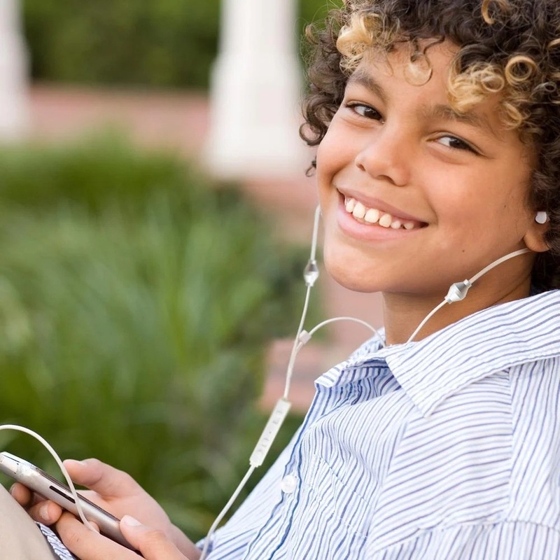 A young person outdoors wearing the white SafeSleeve air tube headphones with the acoustic tubes running to the earpieces