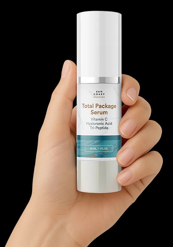 Hand holding the Total Package Serum bottle, showing the Vitamin C, Hyaluronic Acid, Tri-Peptide label