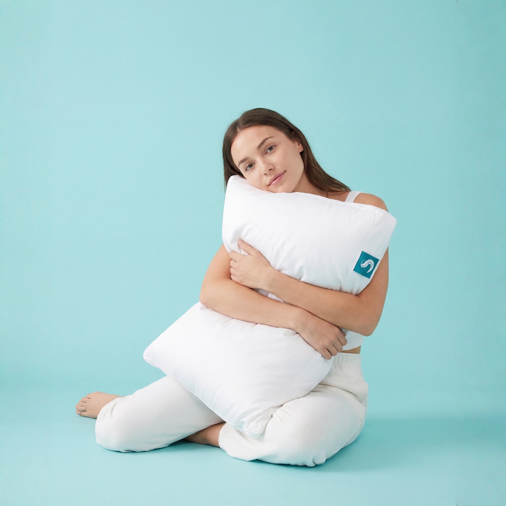 Person hugging a white Sleepgram pillow against a teal studio backdrop