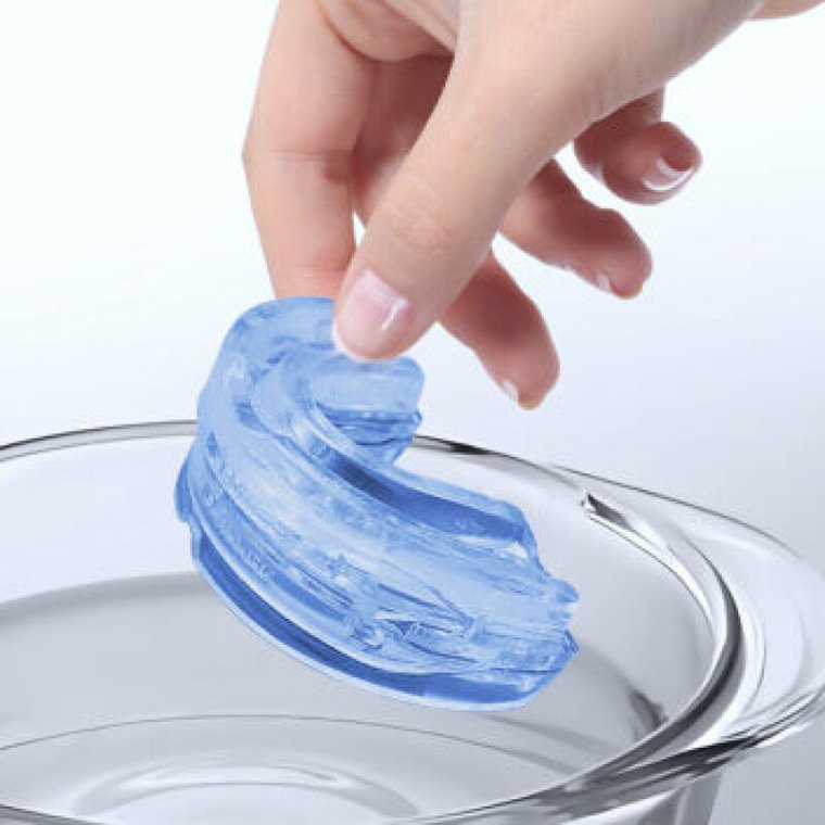 Hand dropping the SleepZee mouthpiece into a bowl of hot water to soften it for molding