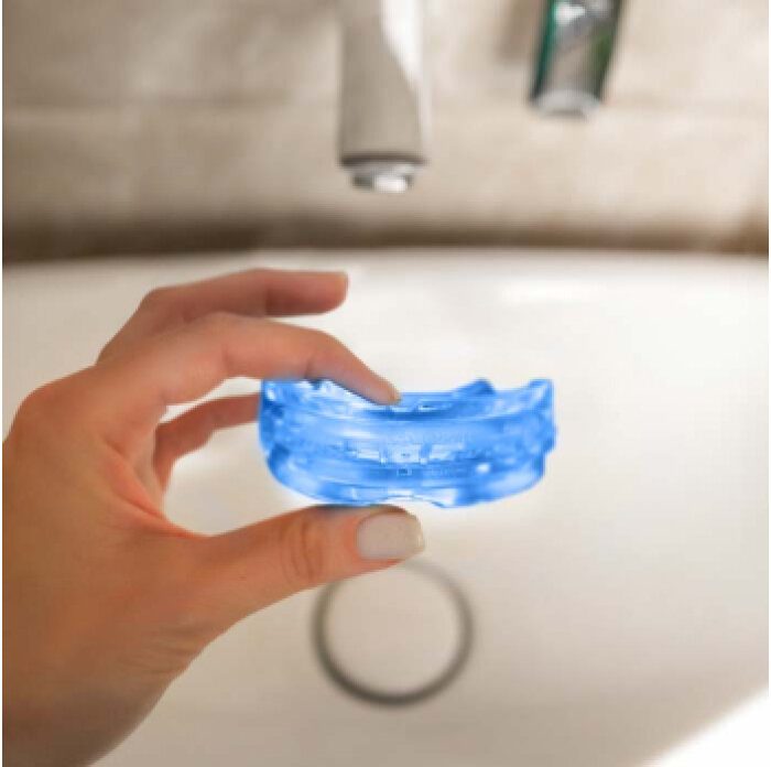 Person holding the SleepZee anti-snoring mouthpiece before molding it at the bathroom sink