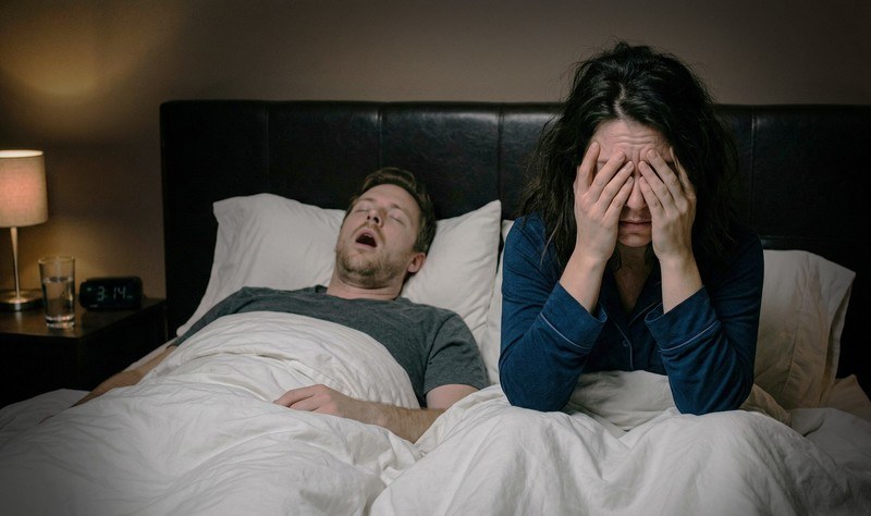 A couple in bed, one person kept awake by the other's snoring