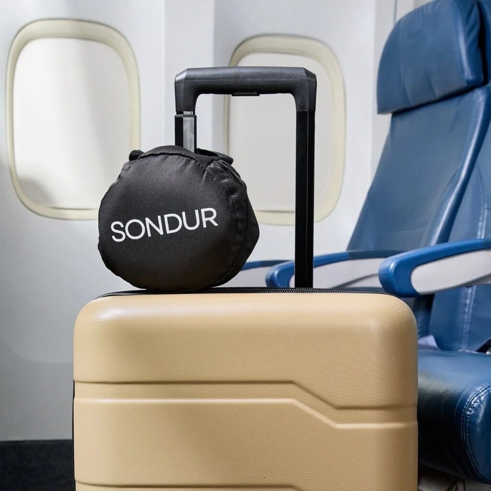 The Sondur travel cushion rolled into its round carry pouch, sitting on top of a suitcase