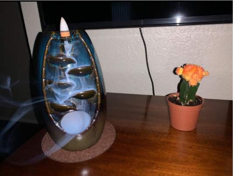 Spirual incense waterfall burner on a wooden table with smoke cascading down its ceramic steps