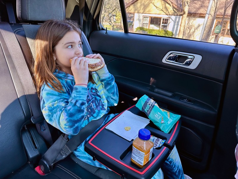 Child eating a sandwich at the Stupid Car Tray holding a drink and snacks in a car