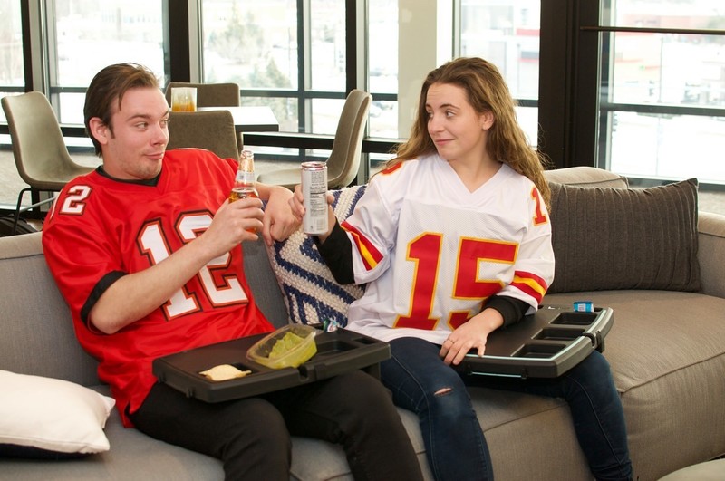 Two people using Stupid Car Trays as lap trays for food and drinks while sitting on a couch