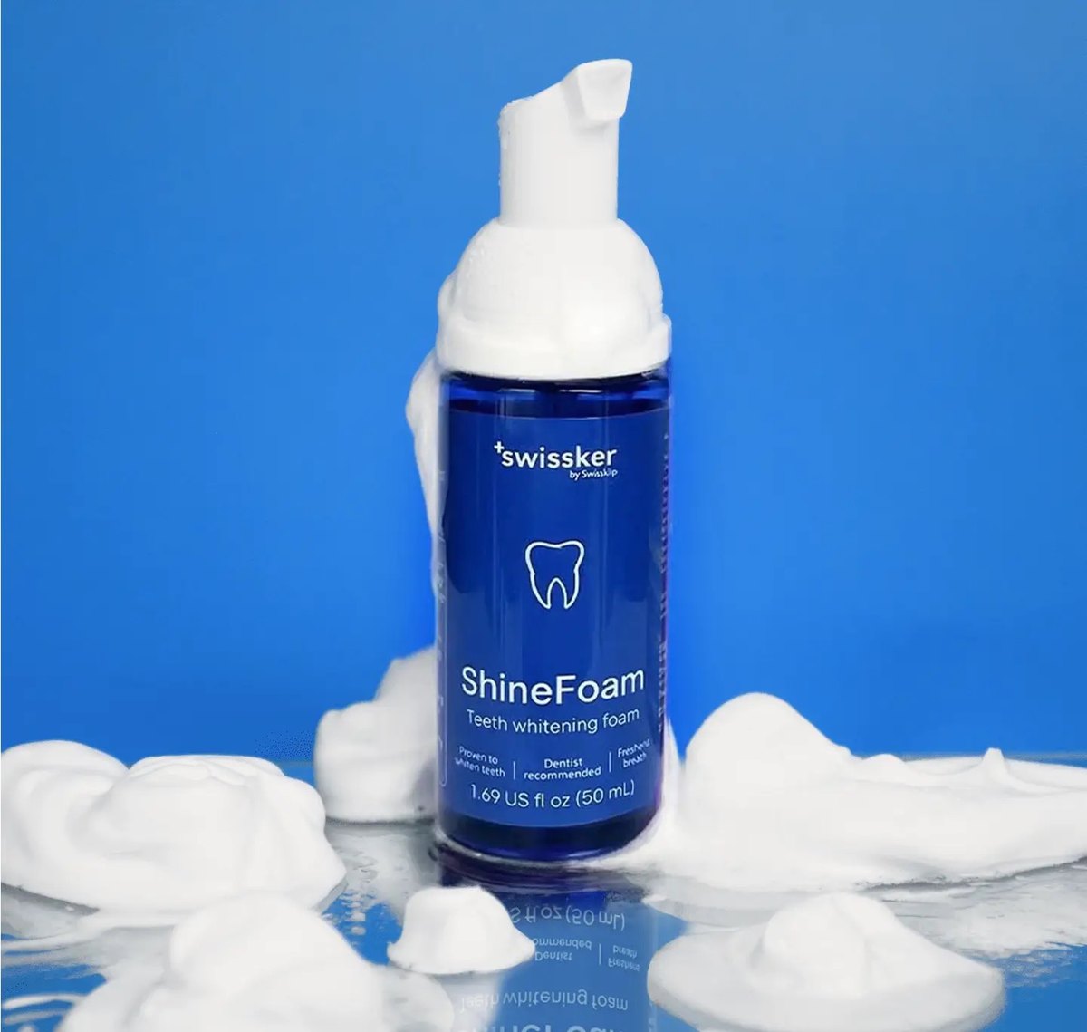 Bottle of Swissklip ShineFoam teeth whitening foam surrounded by dollops of white foam